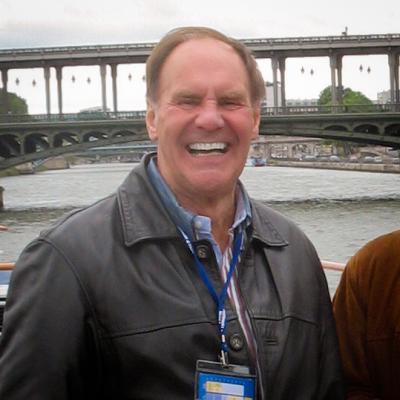 A white man in a leather jacket on a river boat.  He is wearing a leather jacket and smiling broadly.